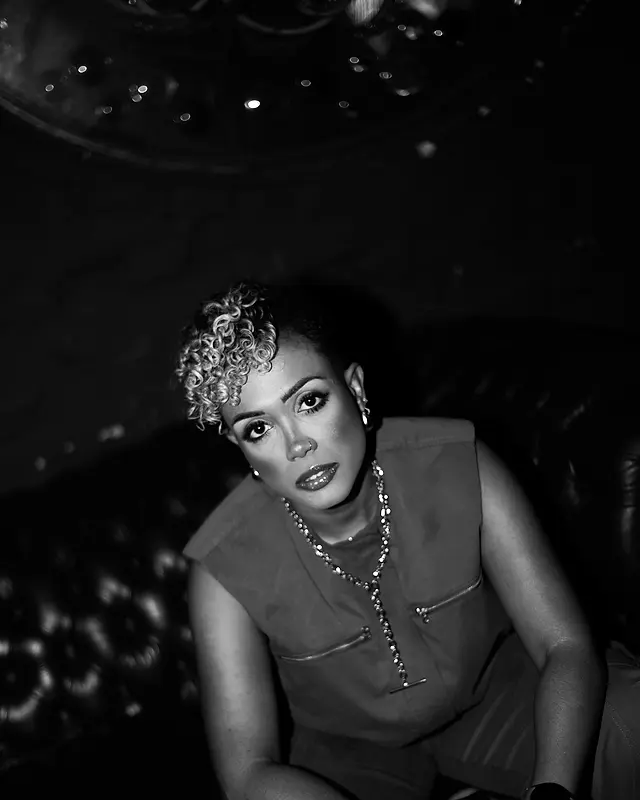 Carol, cantora e idealizadora da Black SP, sentada num sofá de couro, olhando pra câmera