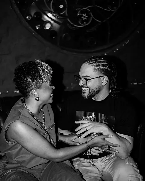 Carol e Daniel rindo juntos, de mãos dadas no sofá