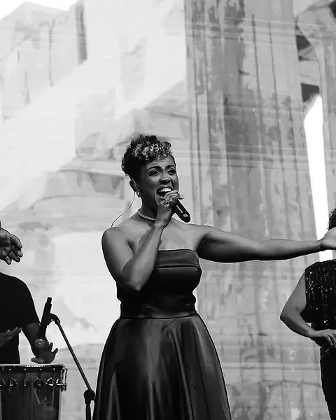 Cantora da Black SP de vestido longo cantando de braço aberto num evento corporativo