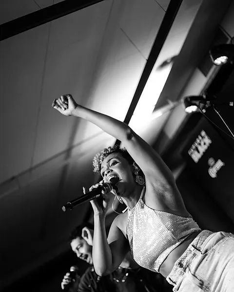 Cantora da Black SP de braço erguido no palco de um evento de empresa