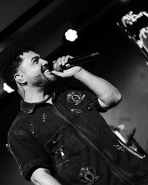 Cantor da Black SP cantando com o microfone erguido, de cabeça pra cima
