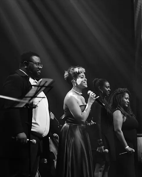 As vozes da Black SP em traje de gala cantando juntas, com o contrabaixo atrás