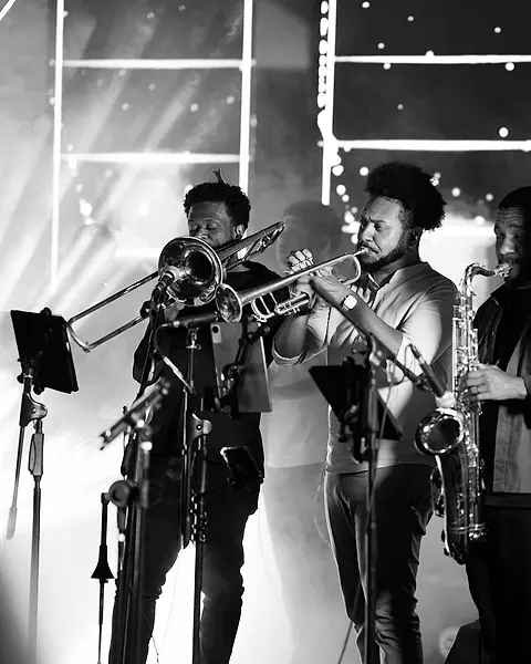 O trio de metais da Black SP tocando trombone, trompete e saxofone contra a luz