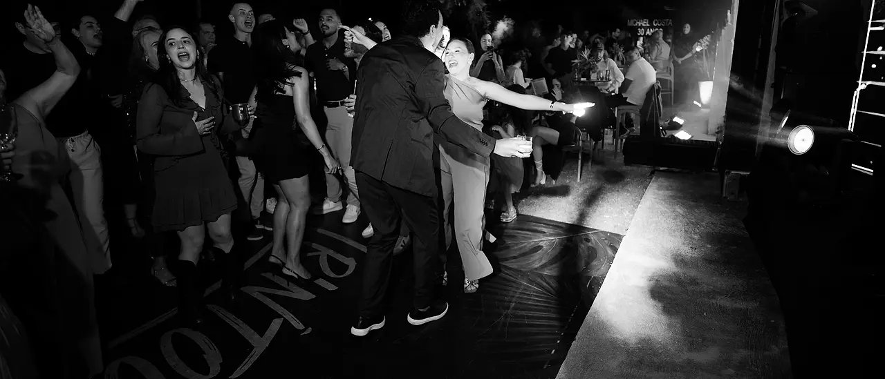 A pista cheia de uma festa, com os convidados dançando sob as luzes do palco